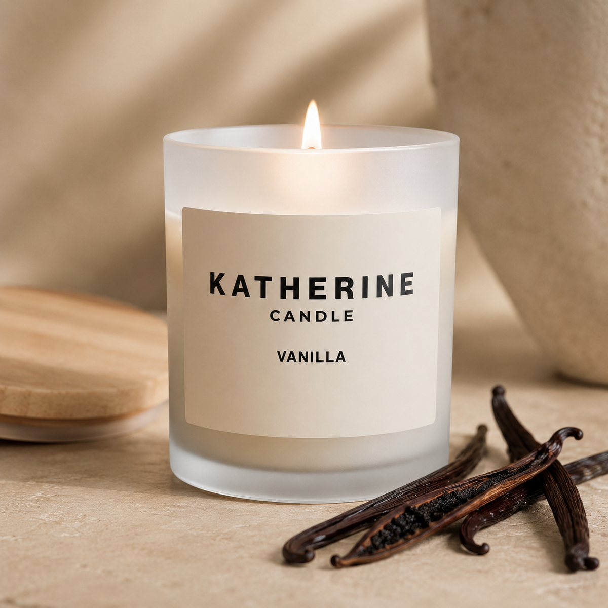 A lit frosted glass candle jar labeled KATHERINE CANDLE VANILLA, set on a beige surface with vanilla beans in the foreground and a soft neutral background.