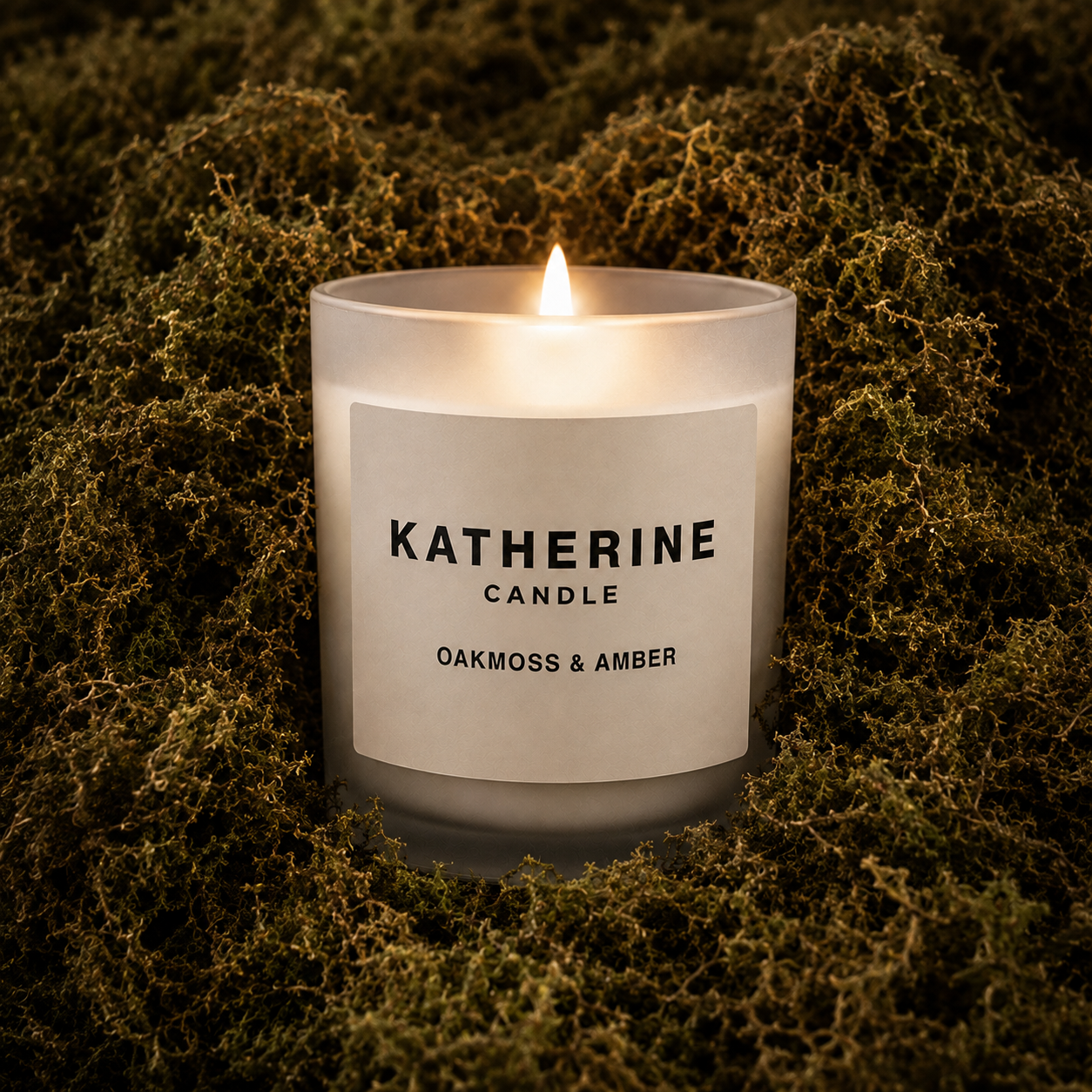 Burning soy wax candle in white jar; KATHERINE label reads OAKMOSS & AMBER