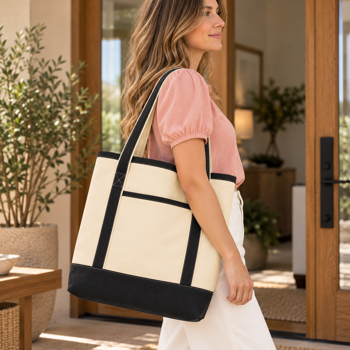 Cream canvas tote with black trim and base, worn over the shoulder; front pocket visible