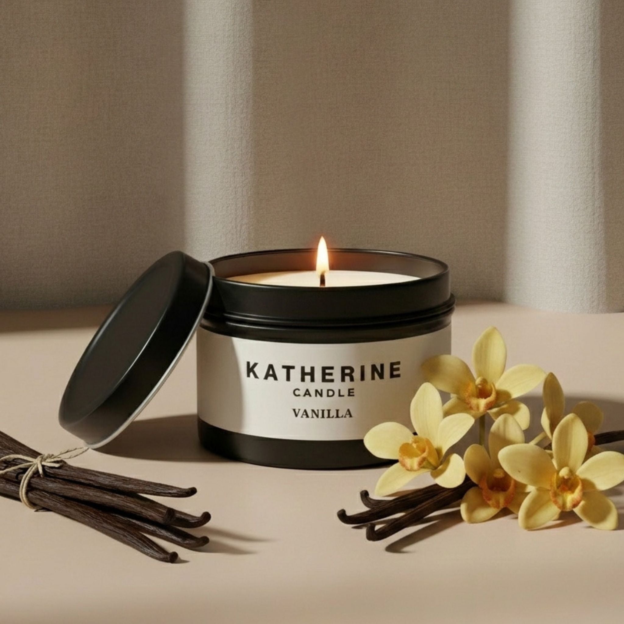 Vanilla scented candle with black lid open, lit wick, vanilla beans and yellow flowers